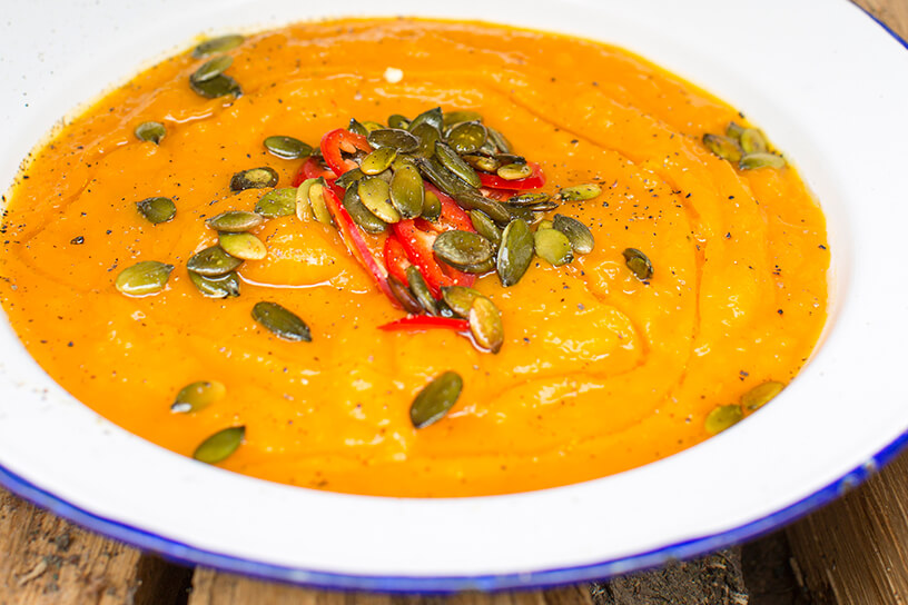 pompoensoep met rode peper en pompoenpitten in diep bord