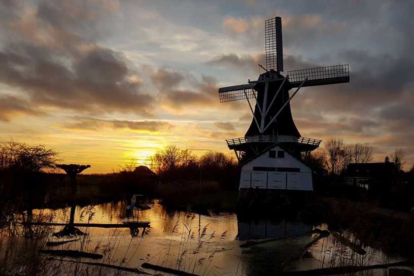 Molen naast het water in de avond, de zon gaat onder 