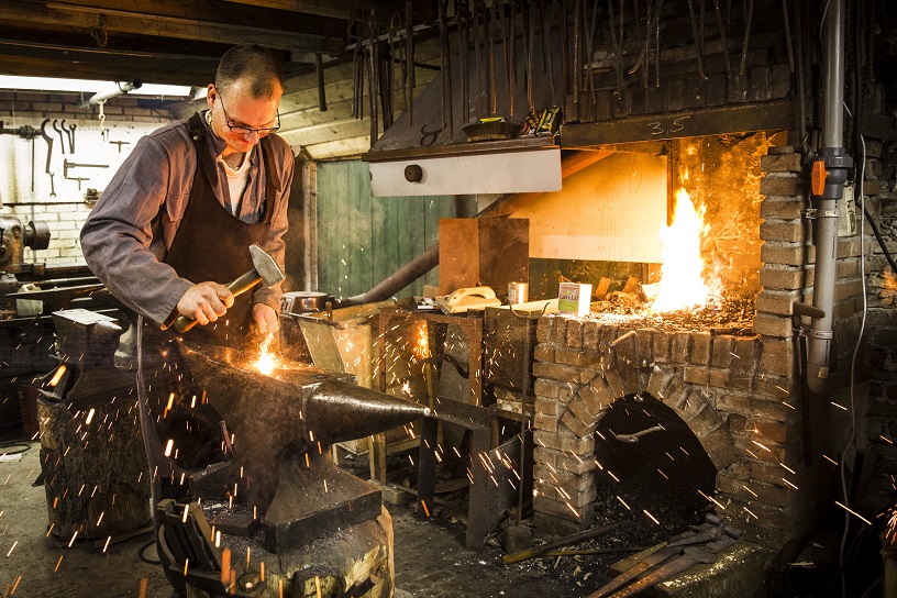 Meneer in werkplaats ijzer aan het smeden