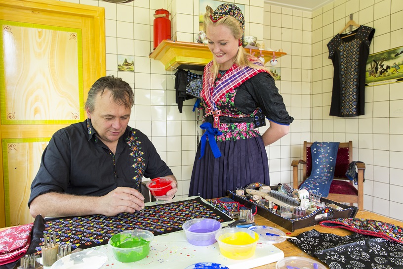 Een mevrouw in klederdracht met een meneer om staphorster stipwerk te maken