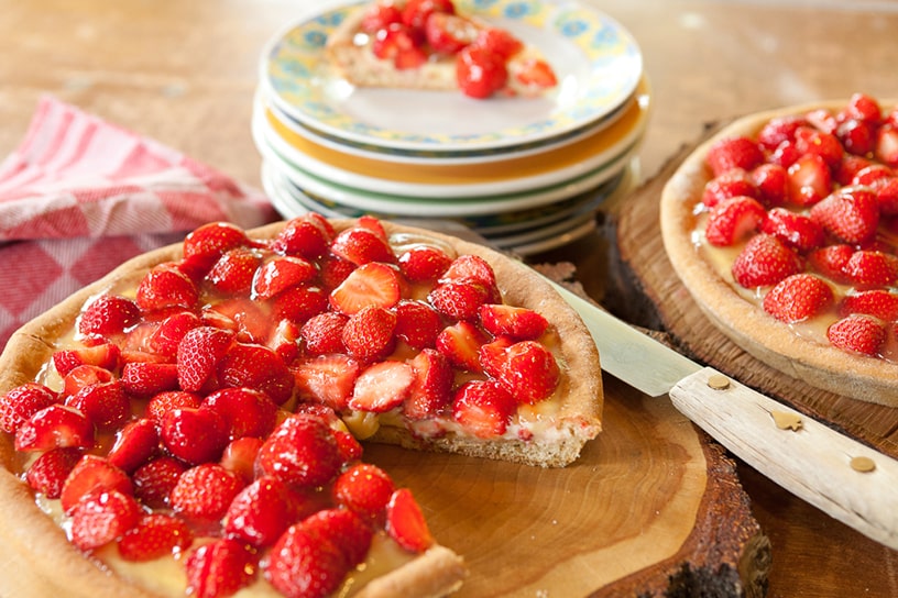 Een aangesneden aardbeienvlaai op een houten plank