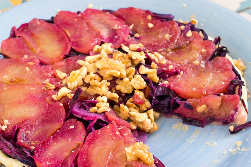 Aangesneden tarte tatin van rode kool bestrooid met walnootjes